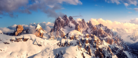 Wall Mural - Snowy mountains in low clouds and blue sky at sunset in winter. Panoramic landscape with beautiful snow covered rocks in fog in frosty evening. Aerial view of high peaks. Alps in Dolomites, Italy
