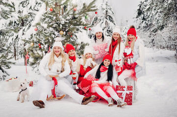 A large group of girls with Christmas gifts in their hands standing in the winter forest.Girls in red and white clothes with Christmas gifts in the snowy forest