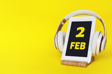 February 2nd. Day 2 of month, Calendar date. Stylish headphones and modern tablet on yellow background. Space for text. Education, technology, lifestyle. Winter month, day of the year concept.