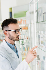 Wall Mural - pharmacist in white coat and eyeglasses pointing with finger in drugstore