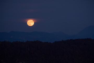 huge orange full moon rising behind a mountain ridge illuminating misty clouds creating a mystical a