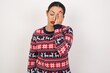 © Roquillo - Tired overworked Young beautiful Arab woman wearing Christmas sweater, against white has sleepy expression, gloomy look, covers face with hand, has eyes shut, gasps from tiredness, fatigue after party