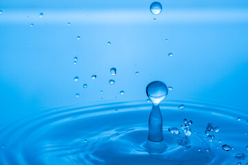 Wall Mural - Water drop splashing into blue water surface