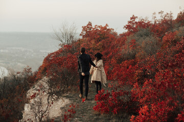 Autumn lovely young couple in stylish clothes is walking on top of hill and holding hands. Autumn time.