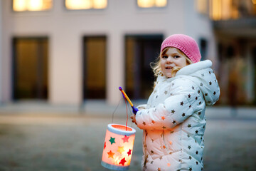 Little kid girl holding selfmade lanterns with candle for St. Martin procession. Healthy cute toddler child happy about children and family parade in kindergarten. German tradition Martinsumzug