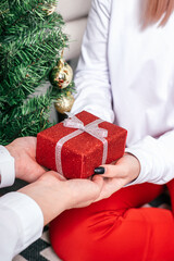 Mom gives a red gift box to her daughter at the Christmas tree, close-up of hands.Family Christmas and New Year concept.