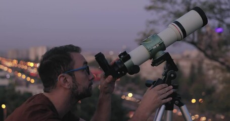 Wall Mural - amateur astronomer looking at the stars with a telescope with blurred city lights in the background.