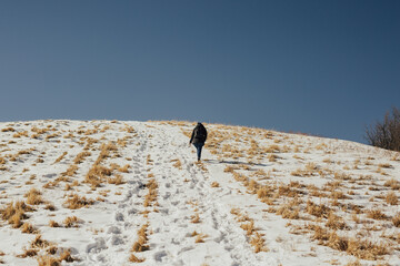 Wall Mural - Back of girl while climbing on the top of mountain. Woman with a backpack walking on snow. Blue sky. Copy space.