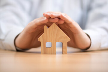 Poster - Wooden toy house protected by hands. Home insurance concept