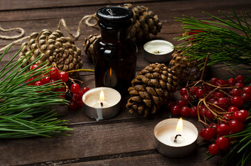 Three little round candles, red viburnum, fir branches and cone, glass bottle on the rustic wooden desk.Comfort and coziness