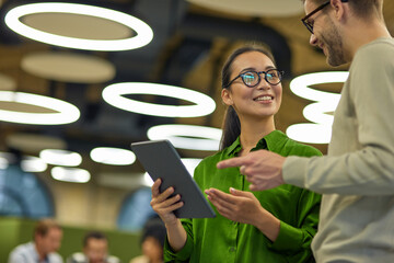 discussing project. young positive asian woman showing something on digital tablet to her male colle