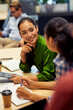 © Friends Stock - Vertical shot of a young cheerful female office worker discussing something with her colleague while sitting at the desk and working together in coworking space or office