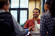 © Friends Stock - Young smiling mixed race male office worker sitting at the desk and talking with colleagues, working together in the modern office