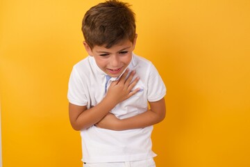 Cute Caucasian little boy standing against yellow background  keeps hands crossed, laughs out loud at good joke, wears casual clothes.