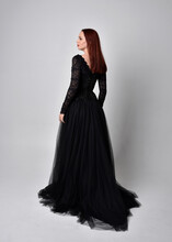 Full Length Portrait Of  Woman Wearing Black Gothic Dress,  Standing Pose  Against A Studio Background.