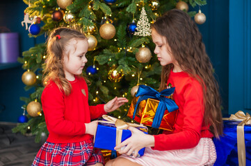 Two cute girls are holding gift boxes in their hands in a Christmas interior with a Christmas tree. Christmas and New Year concept