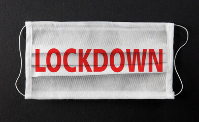 Wall Mural - White face medical mask with word LOCKDOWN printed on it, isolated on black background. Covid-19 outbreak, coronavirus quarantine, lockdown concept