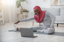 Black Muslim Woman In Hijab Exercising In Front Of Laptop At Home
