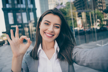Photo of joyful pretty businesswoman wear formalwear suit jacket make selfie okay sign in outdoors center