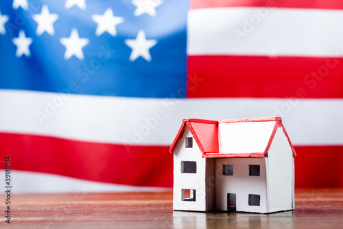 house model on wooden desk near american flag on blurred background