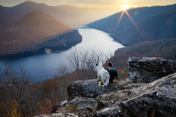 man and his dog sitting on rock enjoying amazing autumn view over lake at sunset