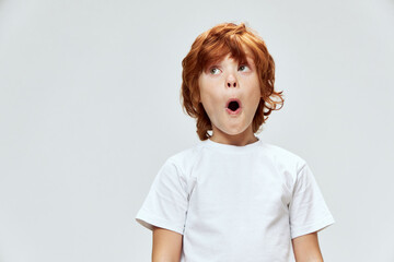 Wall Mural - Surprised red-haired boy with open mouth looks up white t-shirt cropped view