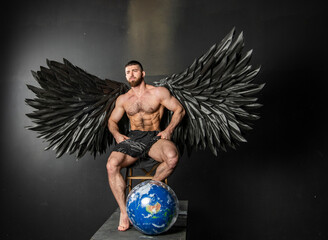 handsome physically well-developed man with black angel wings on a dark background