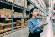 © Dearix - Young energetic smart Asian business working woman smile while using digital tablet to check goods on shelves for product management in warehouse, Logistics business planning concept with copy space