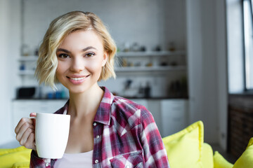 Wall Mural - smiling blonde woman in checkered shirt holding white cup