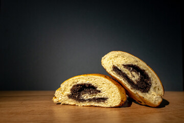 Two cut pieces of a roll with poppy seeds lie on the table on a gray background