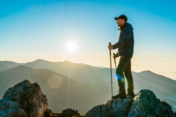 Wall Mural - hiker man standing with trekking poles on a cliff edge and looking at tatra mountains valley covered