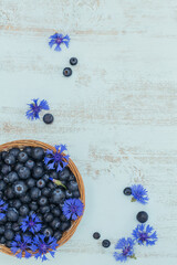 Wall Mural - Fresh blueberries in basket with flowers pattern top view. Healthy food on white table mockup. Delicious, sweet, juicy and ripe berry background with copy space for text