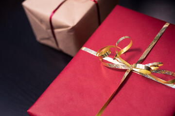 Closeup photography of two presents, a red gift with gold ribbon and a kraft present with red ribbon on dark background.