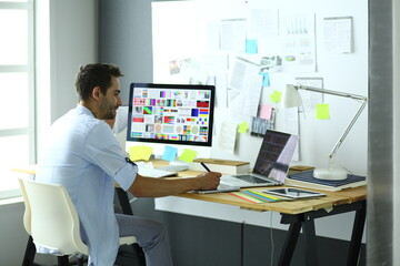 Poster - Portrait of young designer sitting at graphic studio in front of laptop and computer while working online.