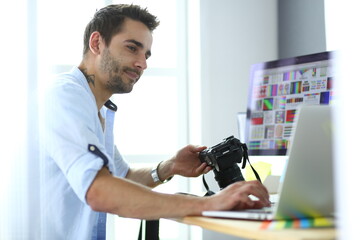 Poster - Portrait of young designer sitting at graphic studio in front of laptop and computer while working online.