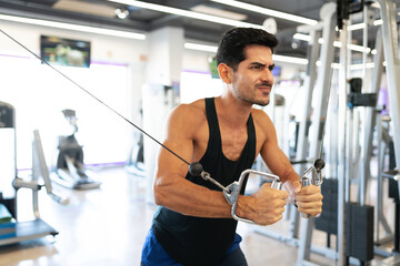 Fit man flexing his biceps with a gym machine