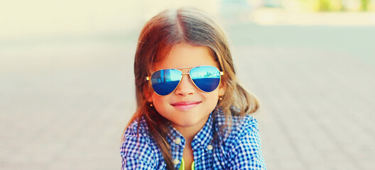 Wall Mural - Portrait of stylish little girl child in the city over a pink background