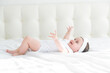 © Юля Шевцова - Cute healthy baby girl 6 months smiling in a white bodysuit lying on a bed on white bedding.