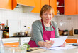 © JackF - Worried elderly housewife sitting in home kitchen, checking utility bills.