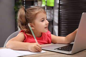 Canvas Print - Cute little girl doing homework with laptop at table