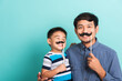 © sorapop - Family funny happy hipster father and his son kid holding black mustache props for the photo booth close face, studio shot isolated on a blue background, November men health awareness
