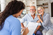 © Zoran Zeremski - Female nurse talking to seniors patients while being in a home visit, senior couple signs an insurance policy.
