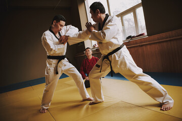 Wall Mural - Two men in white kimono fight in a karate hall.