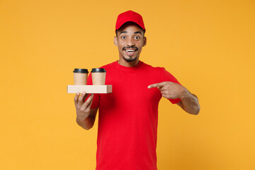 Wall Mural - Delivery employee african man 20s in red cap blank print t-shirt uniform workwear work courier dealer service concept hold takeaway craft brown paper cups coffee isolated on yellow background studio.