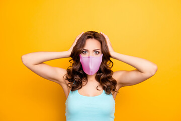 Portrait of irritated woman holding two hands on head wearing pink fabric face mask isolated on yellow background