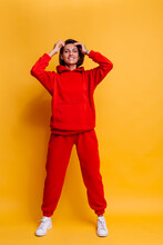 Portrait Of Happy Tanned Fit Caucasian Woman Wearing Trendy Warm Red Fleece Hoodie And Pants, Getting Ready For Cold Winter. Studio Bright Shot, Yellow Background.  