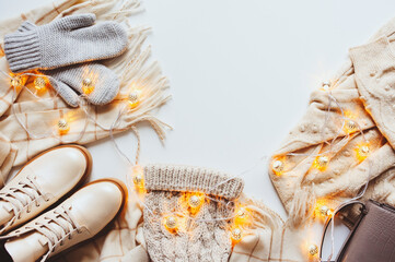 Wall Mural - winter and Christmas sale concept. Woman fashion trendy clothes set with lights top view. Shoes, sweater and knitted hat in white tones