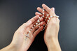 © Andriy - Praying on the rose garden, the hands of a young virgin with a rosary close-up on a black background.