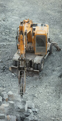 Wall Mural - Hydraulic hammer destroys stones in a stone quarry close-up, view from above, vertical panorama.