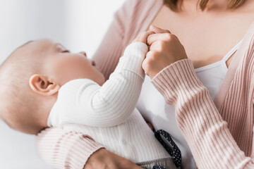 close up of caring woman holding hands with infant boy on blurred background